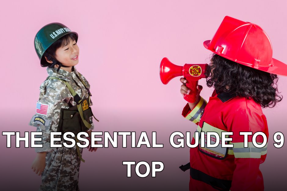 Side view of multiethnic kids wearing navy uniform and firefighter costume with loudspeaker standing together on pink background in hardhats and looking at each other