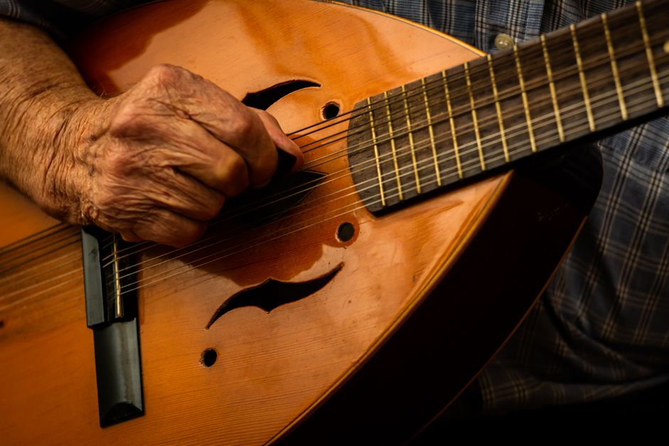 Close-up of an elderly hand strumming a mandolin, emphasizing texture and music.
