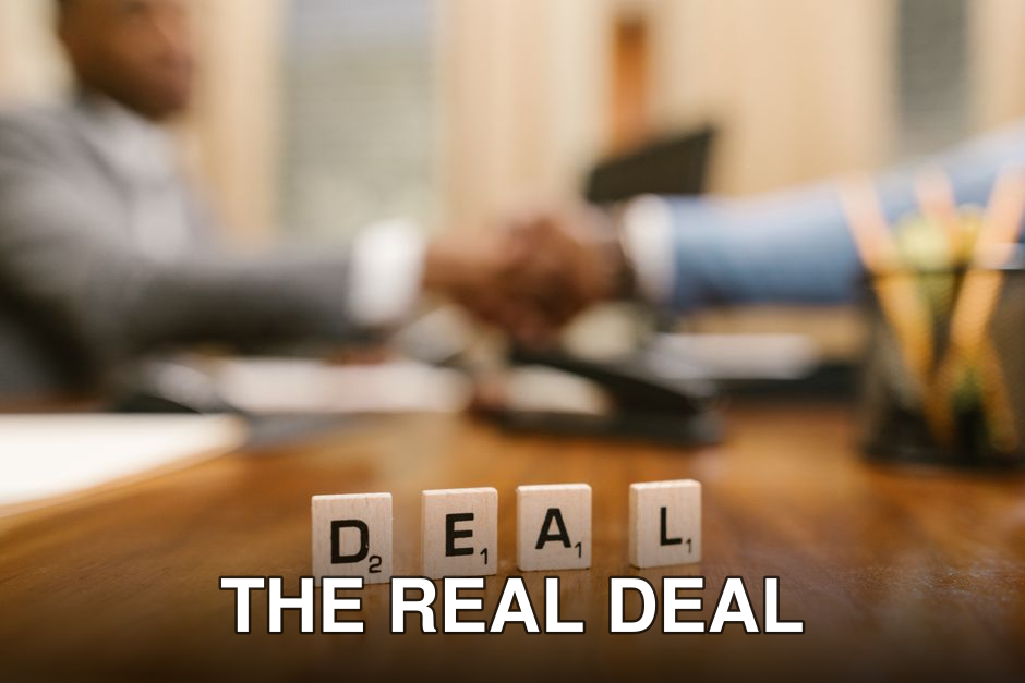 Close-up of Scrabble tiles spelling 'deal' with a handshake in the background.