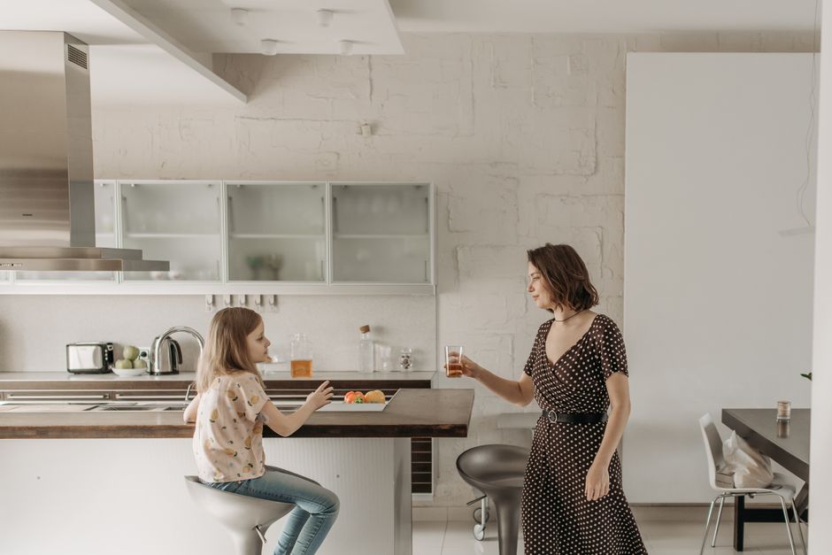 A woman and young girl share drinks and snacks in a stylish kitchen setting.